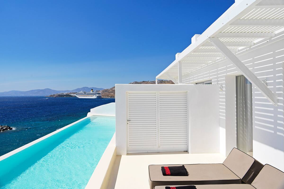 A poolside area with a view of the sea and a cruise ship in the distance.