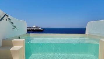 A clear blue pool with steps leading down to the water, a railing on the left, and a cruise ship in the distance.