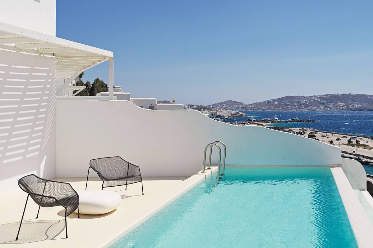 A rooftop infinity pool with a view of the sea and a white building.