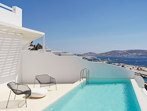 A rooftop infinity pool with a view of the sea and a white building.