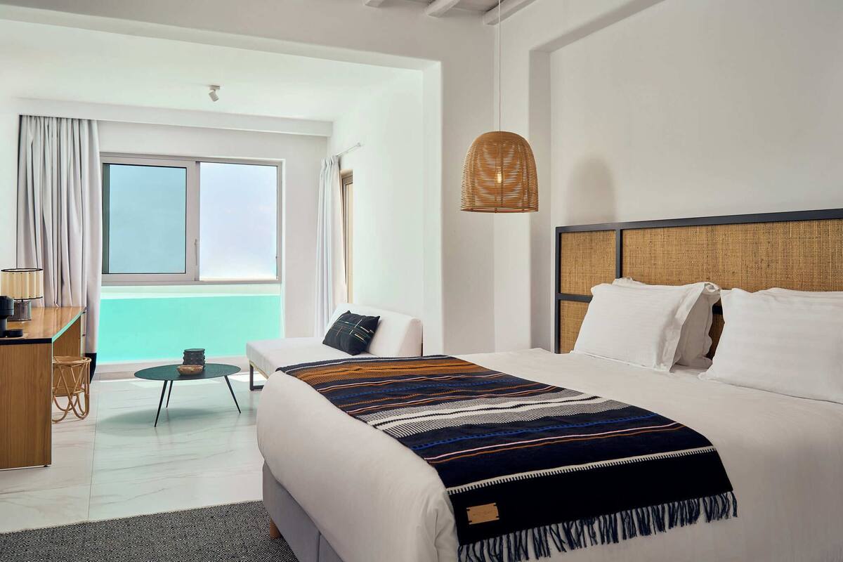 A hotel room with a large bed, a desk, a chair, and a view of the sea through a window.