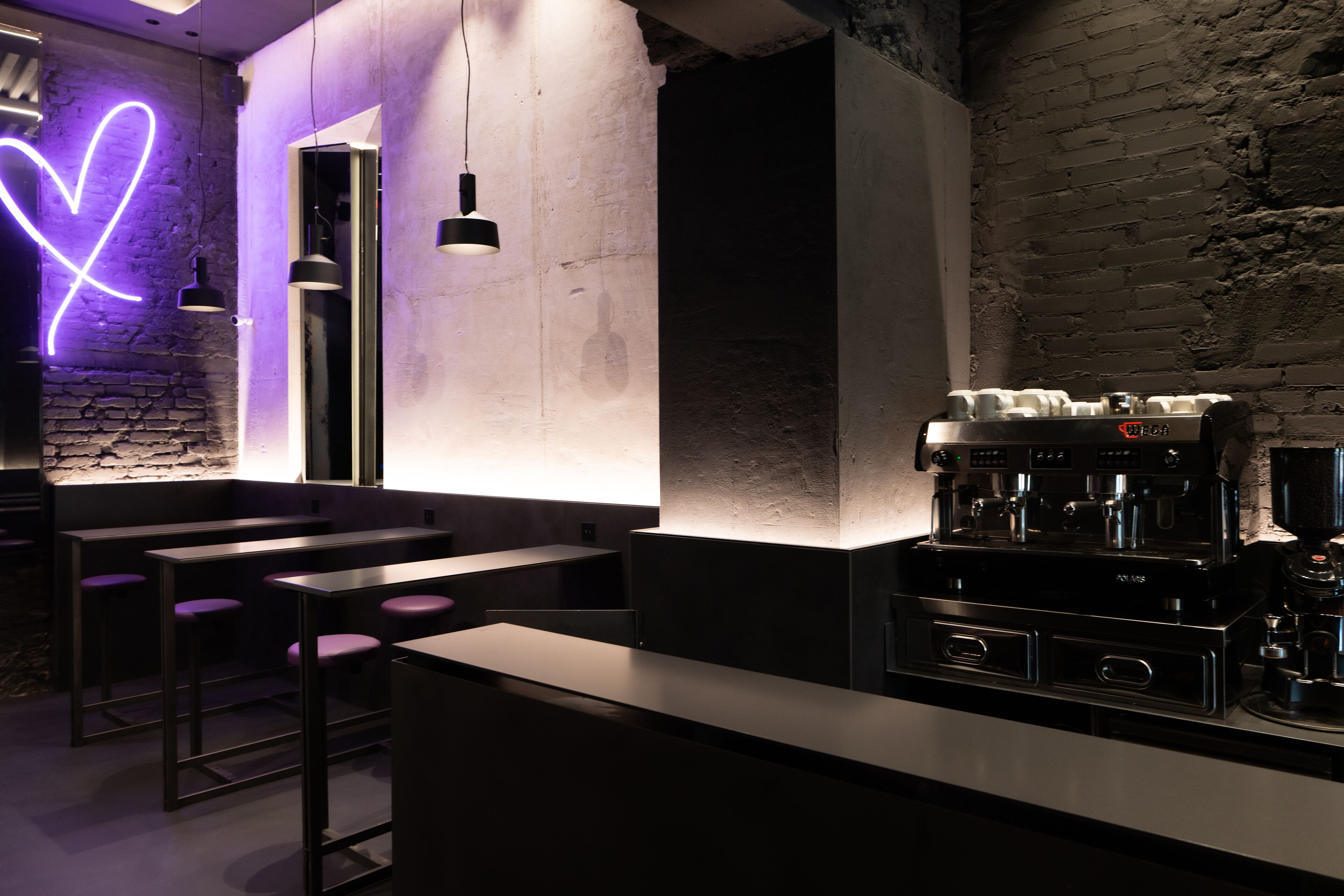 Een moderne bar met een neon hart, barkrukken en een koffieapparaat.