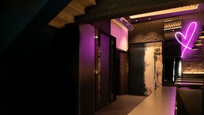 Un couloir faiblement éclairé, orné d’un néon en forme de cœur, avec un plafond en bois et un espace cuisine moderne.