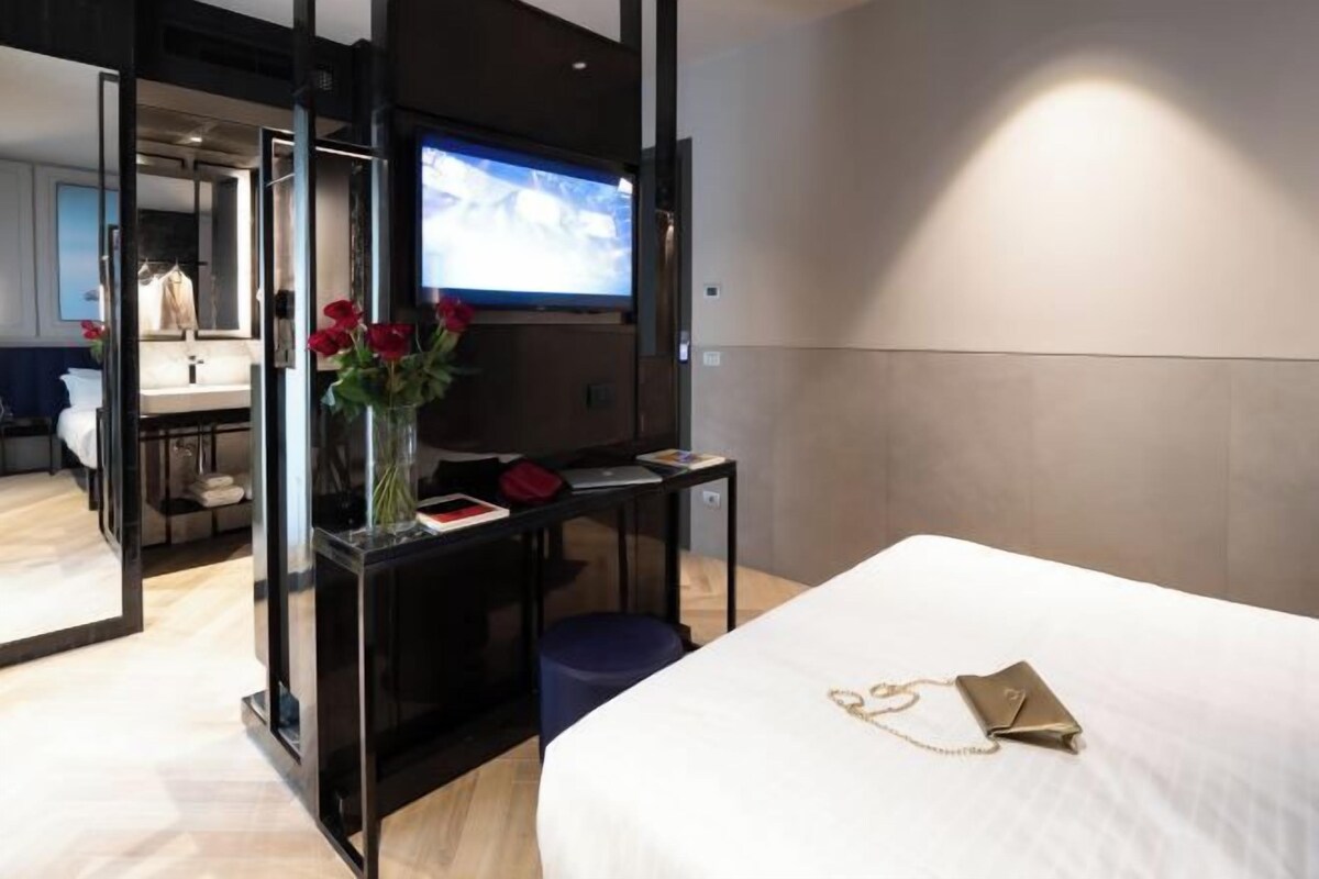 A hotel room with a bed, a desk with a computer, a TV, and a vase with flowers.