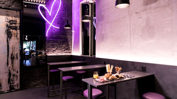 L’intérieur d’un restaurant moderne, avec un néon en forme de cœur, des sièges violets et une table dressée avec de la nourriture et des boissons.