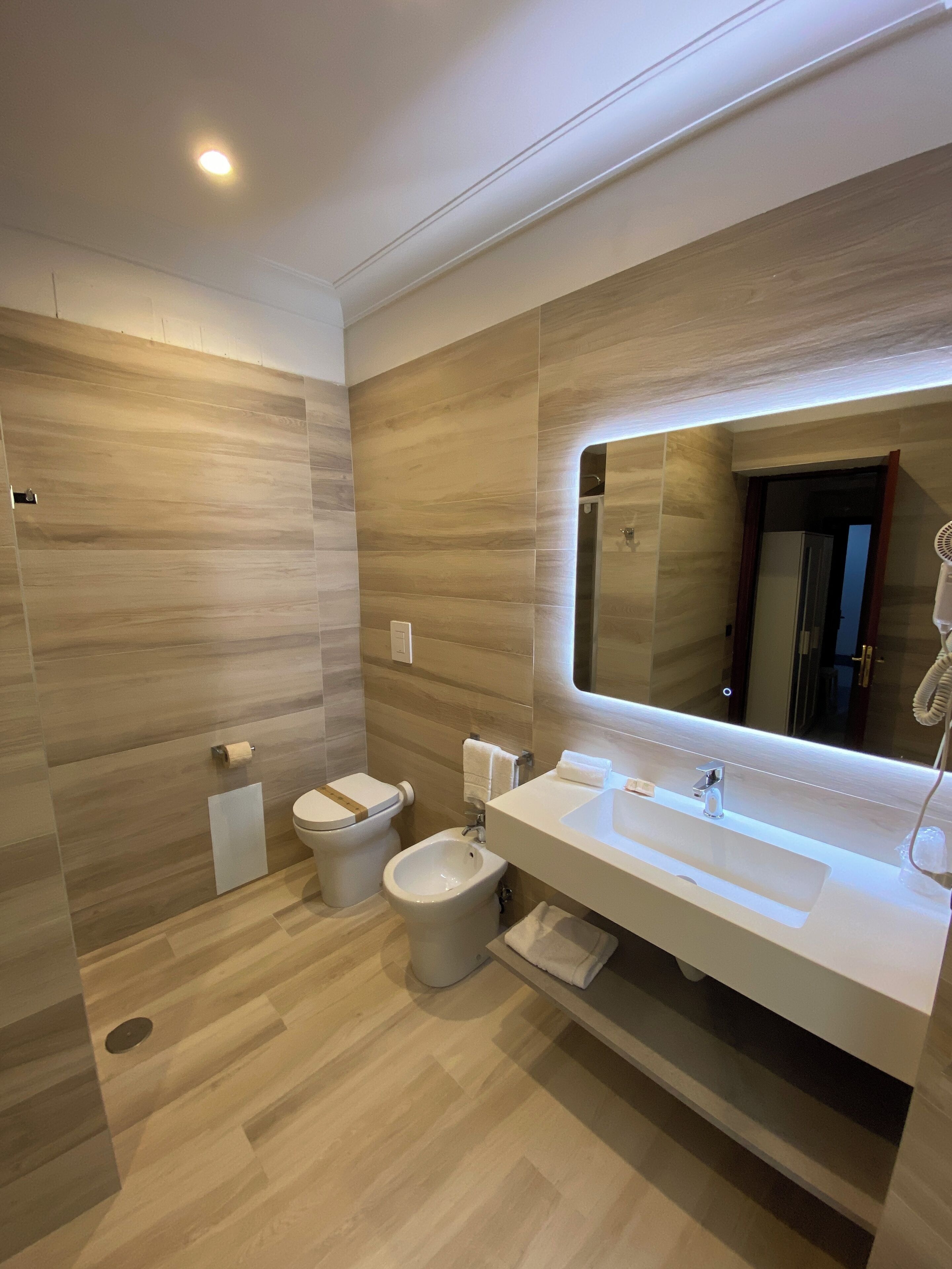 Un bagno moderno con uno specchio grande, un water, un bidet e un lavandino.