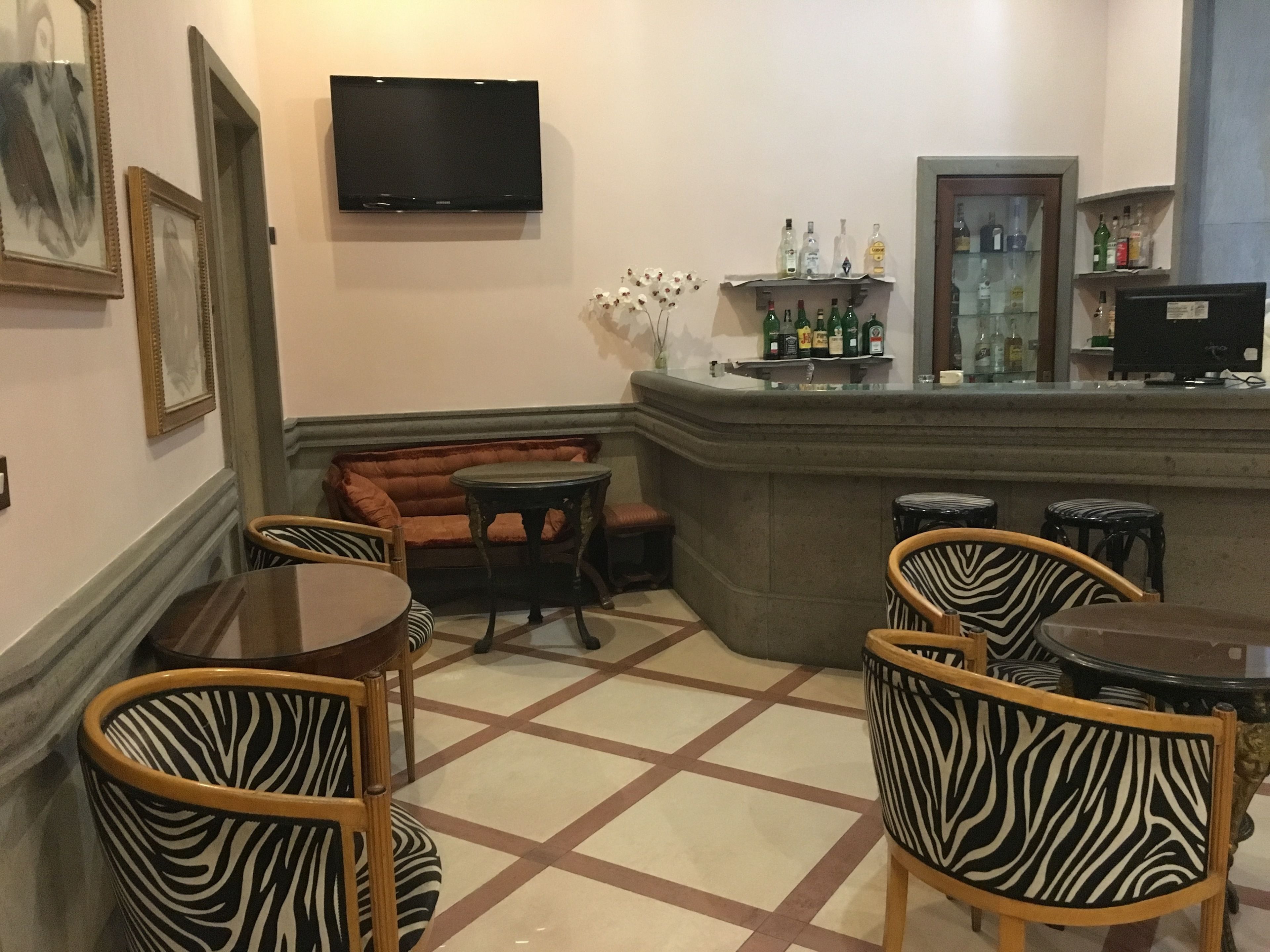 A bar area with a sofa, zebra-patterned chairs, a television, and a display of liquor bottles.