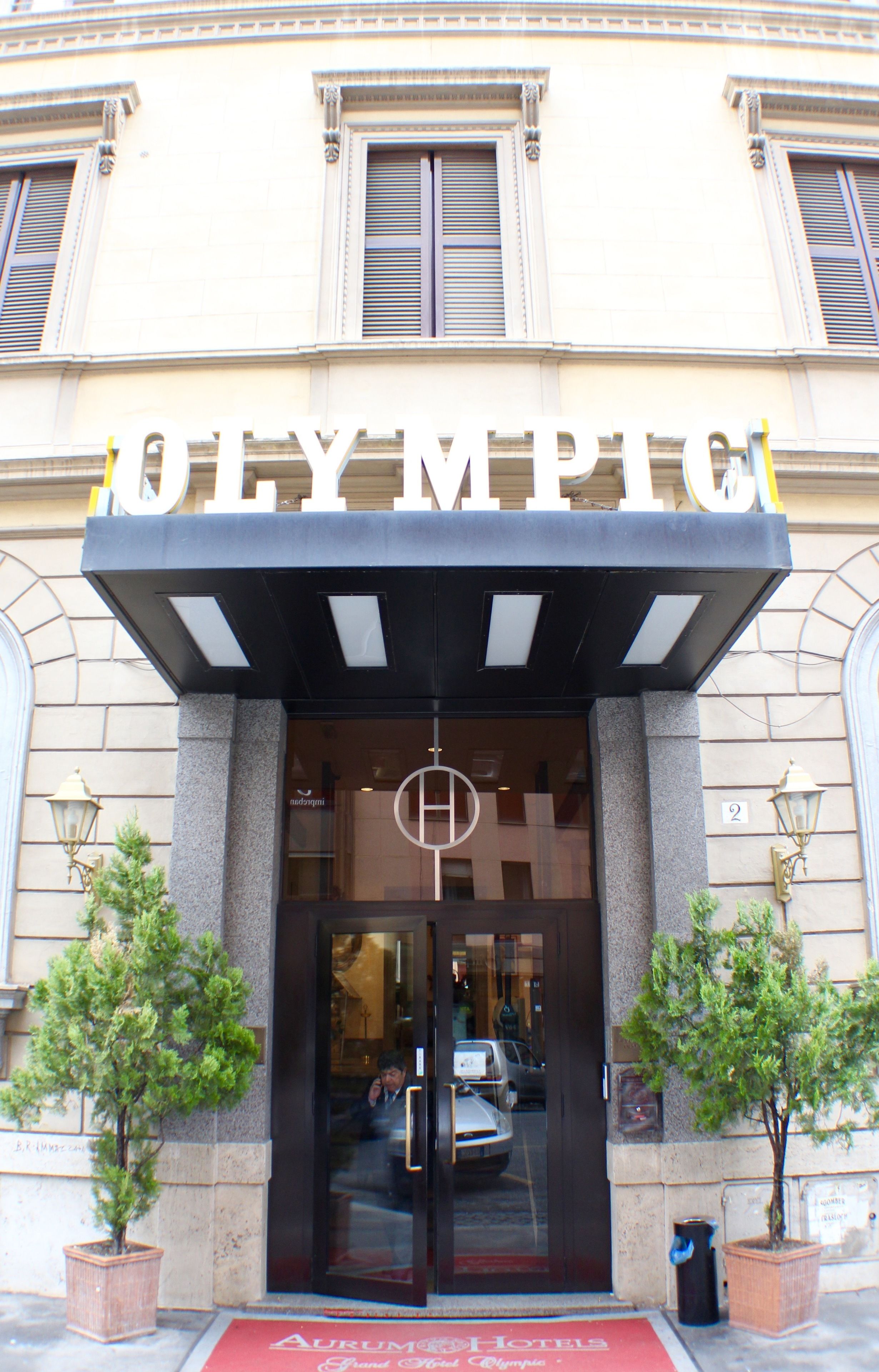 The entrance to the Olympiac Hotel with a black canopy and a glass door.
