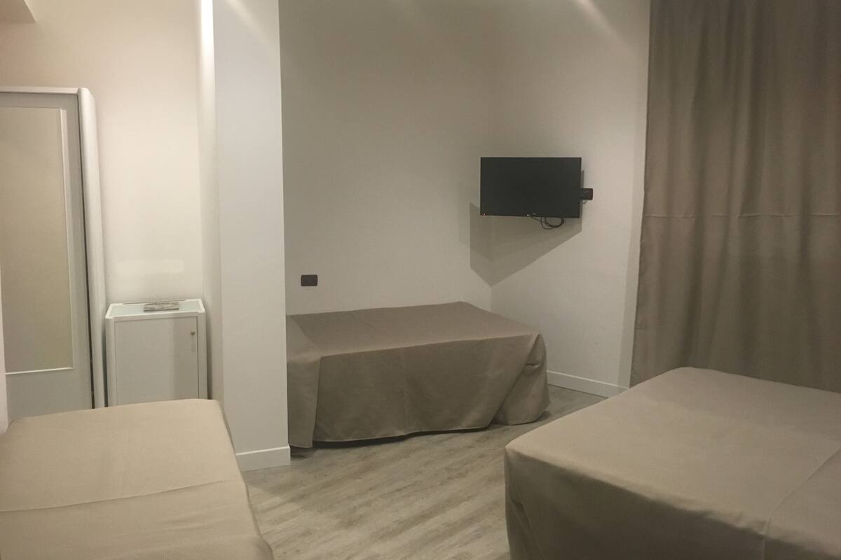 Quarto com duas camas, televisão presa na parede, uma mesinha e uma porta.
