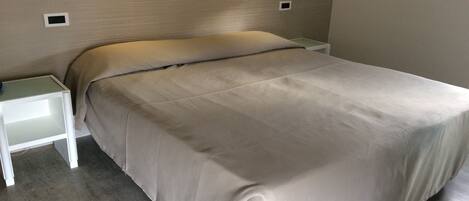 A bedroom with a bed, a nightstand, and a wall-mounted light fixture.