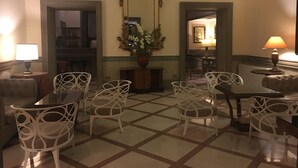 A hotel lobby with a checkered floor, white chairs, a central mirror, and a dining area with a table and chairs. - Grand Hotel Olympic (Rome)