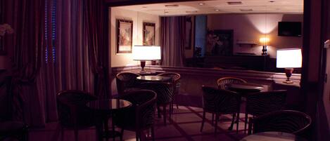 Una habitación de hotel tenuemente iluminada con una zona de bar, varias sillas y una mesa redonda.