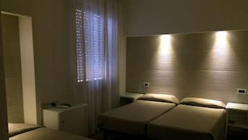 Una camera d'albergo con due letti singoli, un tavolino accanto al letto e una finestra con tende.