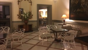 A hotel lobby with a checkered floor, white chairs, a sofa, a table, a mirror, and a painting on the wall. - Grand Hotel Olympic (Rome)