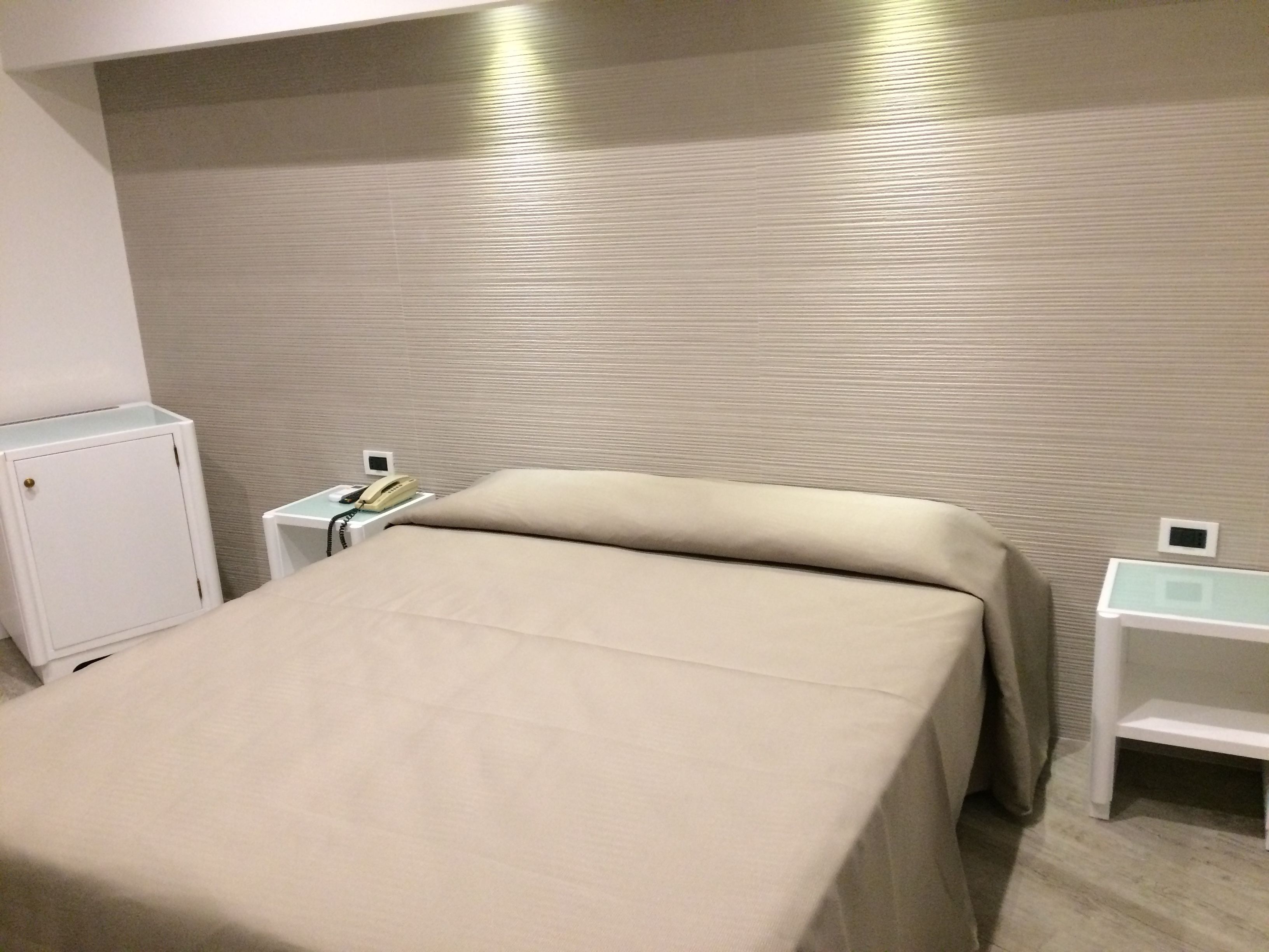 A hotel room with a bed, a bedside table with a phone, and a small cabinet.