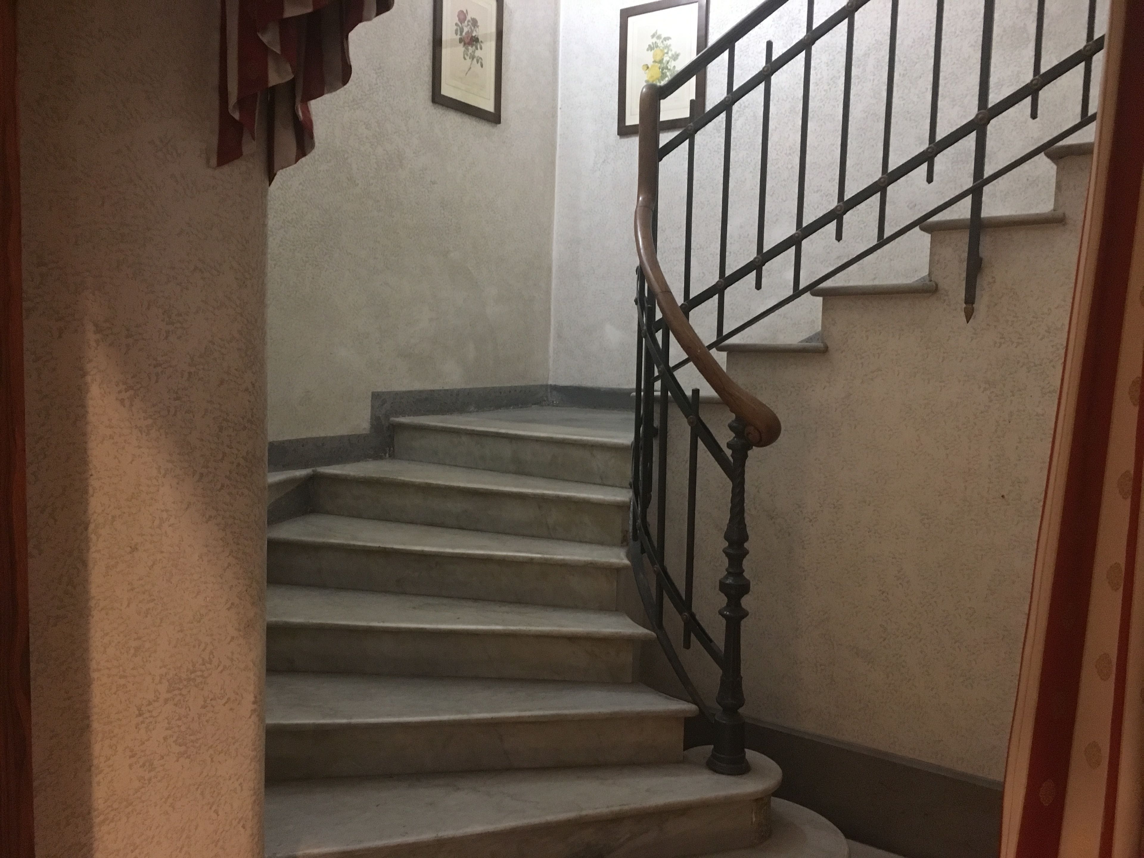 A staircase with a wooden handrail and metal balusters, leading to a landing with a framed picture.