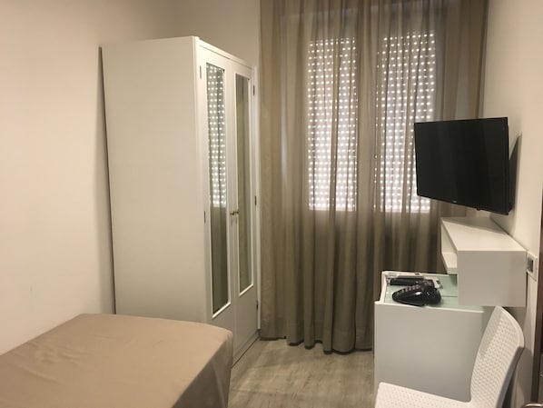 Habitación de hotel con cama, escritorio con televisor de pantalla plana, armario y ventana con cortinas.