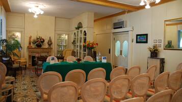 Un salón de conferencias con una mesa verde, sillas de mimbre, una chimenea y un espejo grande en la pared.