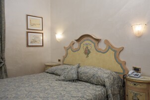 Un dormitorio con una cama, dos cuadros en la pared, una mesita de noche con un tel éfono y apliques de pared.