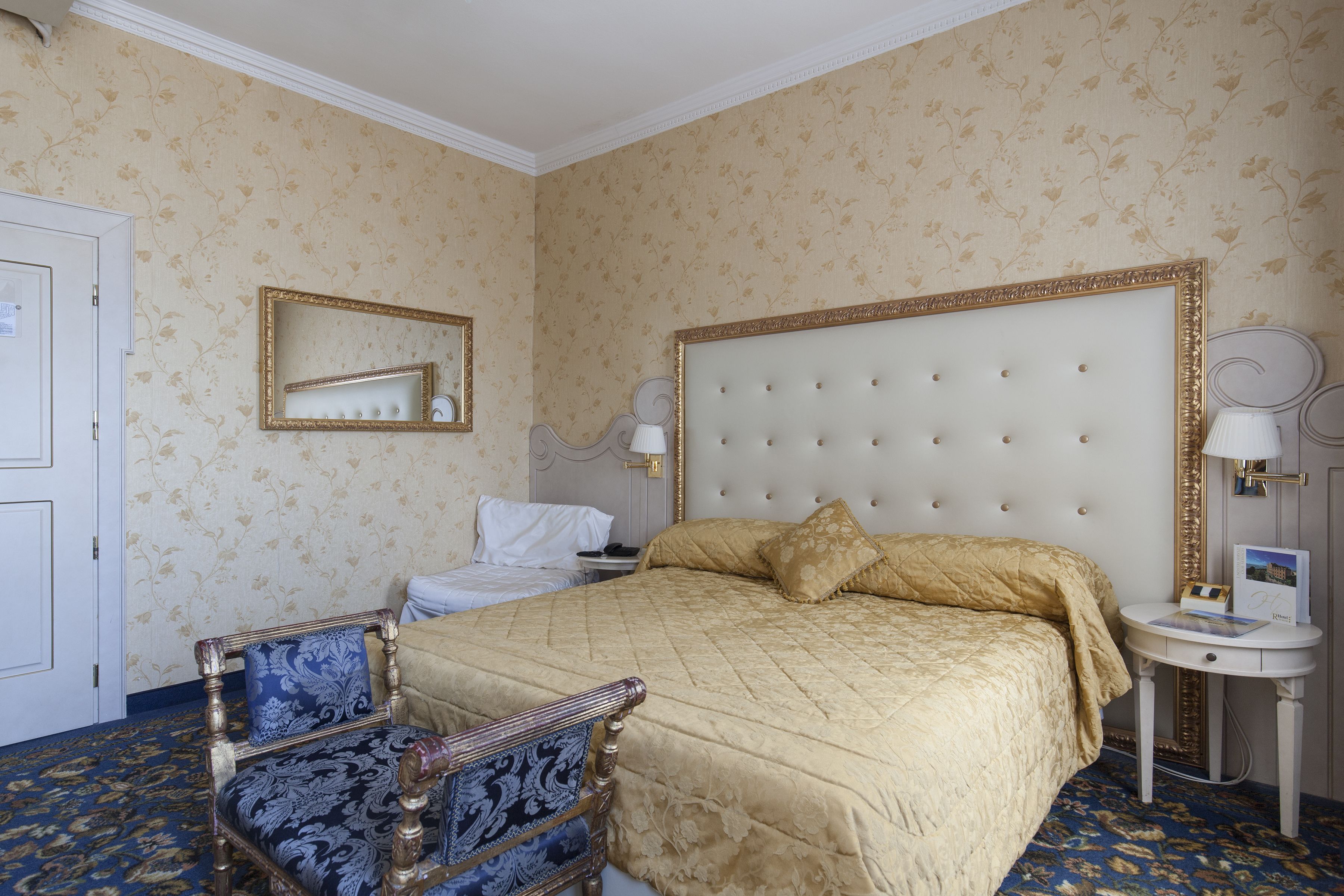 Una stanza con un letto grande, una sedia, un comodino e uno specchio.