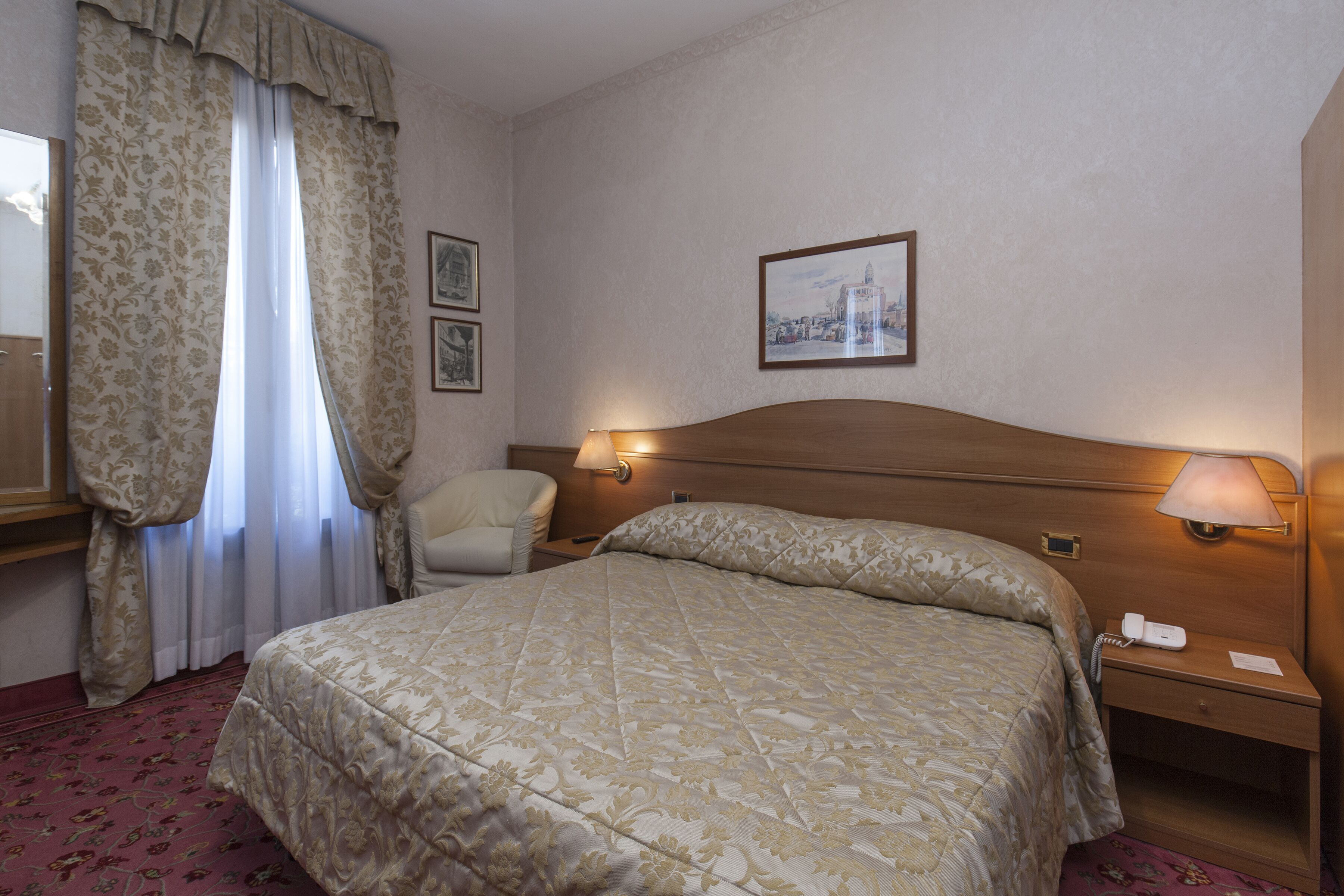 A hotel room with a large bed, a chair, a nightstand with a lamp, and a framed picture on the wall.