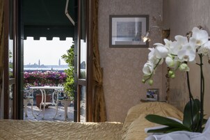 Una habitación con cama, ventana con cortinas, un cuadro enmarcado en la pared y una orquídea en maceta.