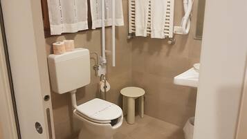 Ein modernes Badezimmer mit Toilette, Bidet, Handtuchhalter und einem kleinen Waschbecken.