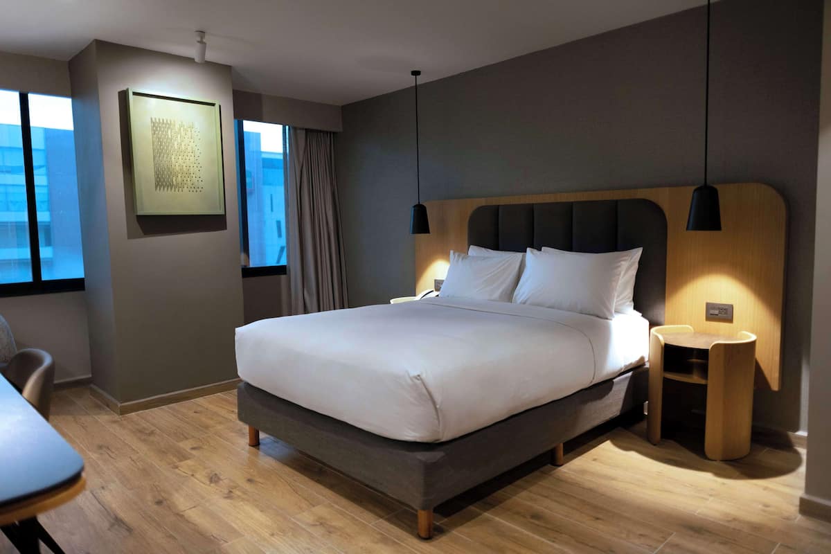 Una habitación de hotel moderna con una cama grande, mesitas de noche, un escritorio y una silla.