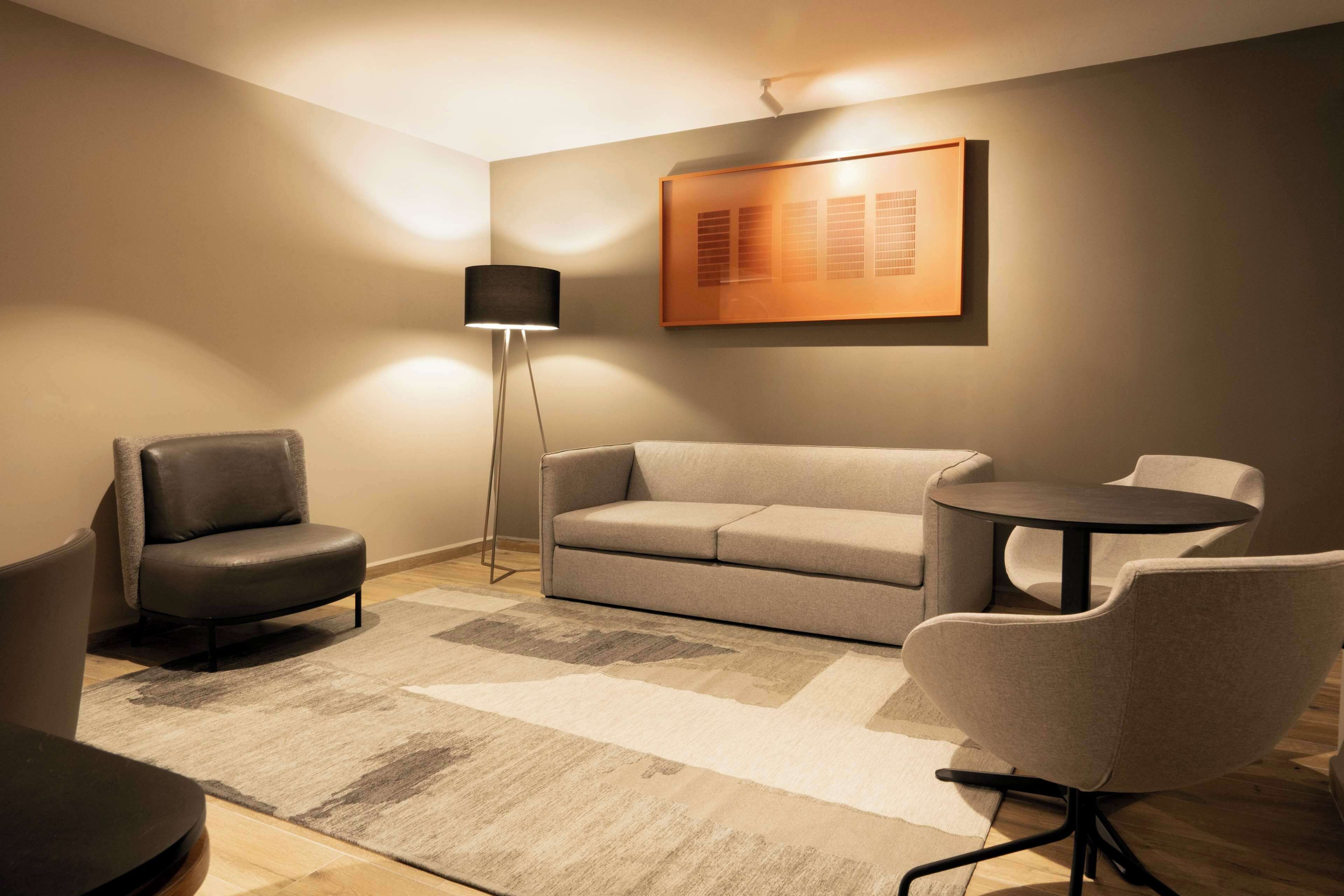 Una sala de estar moderna con un sofá, dos sillones, una mesa de centro y una lámpara de pie.