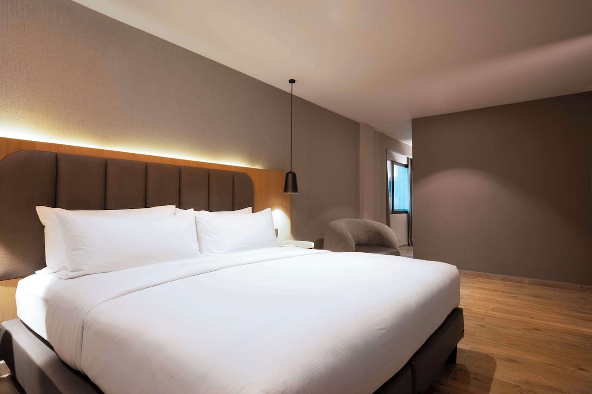 Una habitación de hotel moderna con una cama grande, cabecera con iluminación integrada, mesita de noche y una silla.
