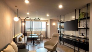 A modern lounge area with a sofa, armchair, round table, and a decorative shelf with items.