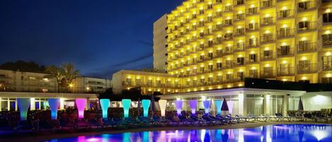 A large hotel with multiple balconies and a pool area with lounge chairs.