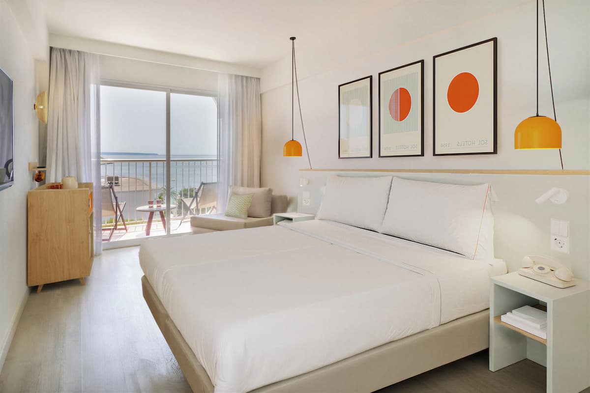 Una habitación de hotel moderna con una cama grande, un balcón con vistas y una pequeña mesa con un teléfono.
