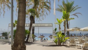 A beach club entrance with palm trees, lounge chairs, and umbrellas. - Sol House Mallorca - Adults only (Calvia)