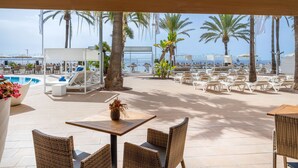 A poolside area with lounge chairs and tables, palm trees, and a view of the sea. - Sol House Mallorca - Adults only (Calvia)