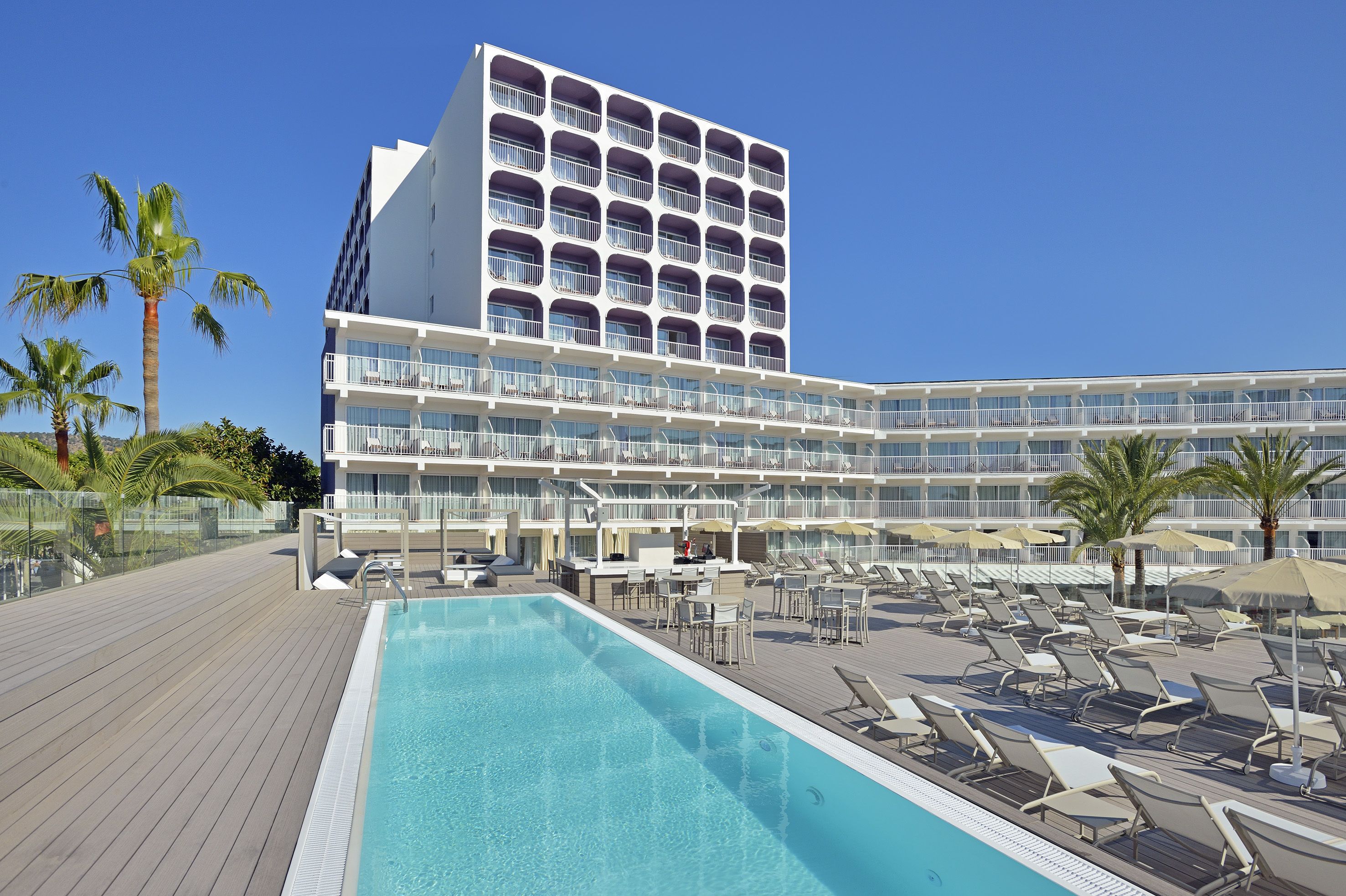 Un hotel con zona de piscina, varios balcones y palmeras.