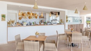 A restaurant with wicker furniture, a wooden bar, and hanging light fixtures. - Sol House Mallorca - Adults only (Calvia)