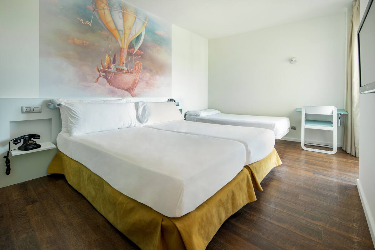 A hotel room with a large bed, a smaller bed, a desk, and a chair.