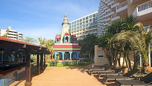 A hotel with a colorful temple-like structure in the center, a pool area with lounge chairs, and a modern building in the background. - Sol Katmandu Park & Resort (Calvia)