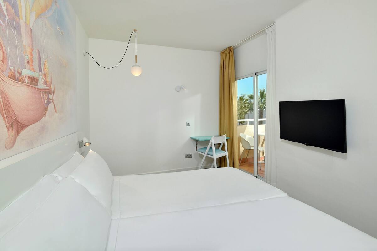A hotel room with a bed, a desk, a chair, a TV, and a balcony with a view.