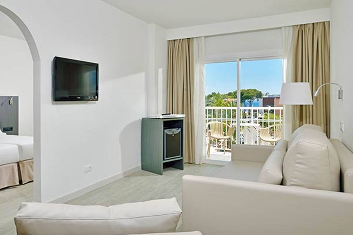 A hotel room with a bed, a TV, a TV stand, a sofa, and a balcony with a view.