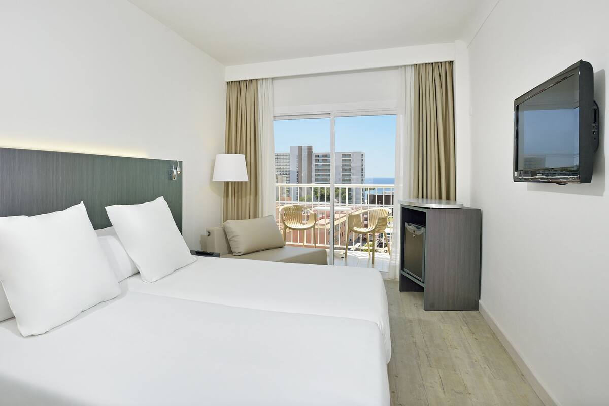 A hotel room with a large bed, a TV, a balcony with a chair, and a view of the city.