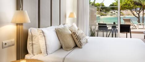 A hotel room with a bed, a bedside table with a candle, a lamp, and a view of a pool and beach.