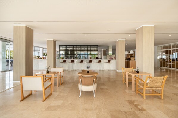 A modern hotel lobby with a central seating area, a bar, and a view of the kitchen in the background. - Melia Calviá Beach (Calvia)