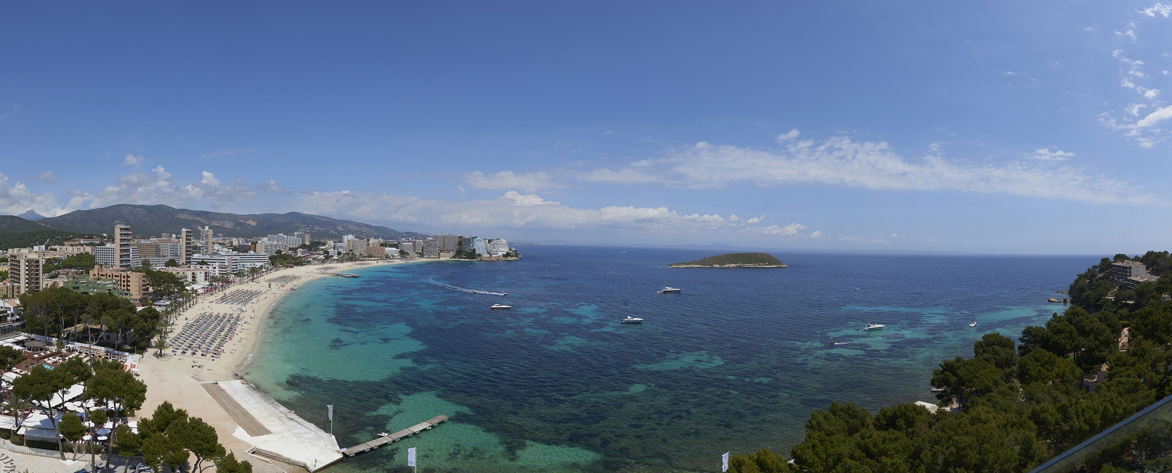 Un paysage urbain côtier avec une plage, une eau d’un bleu limpide et une petite île.