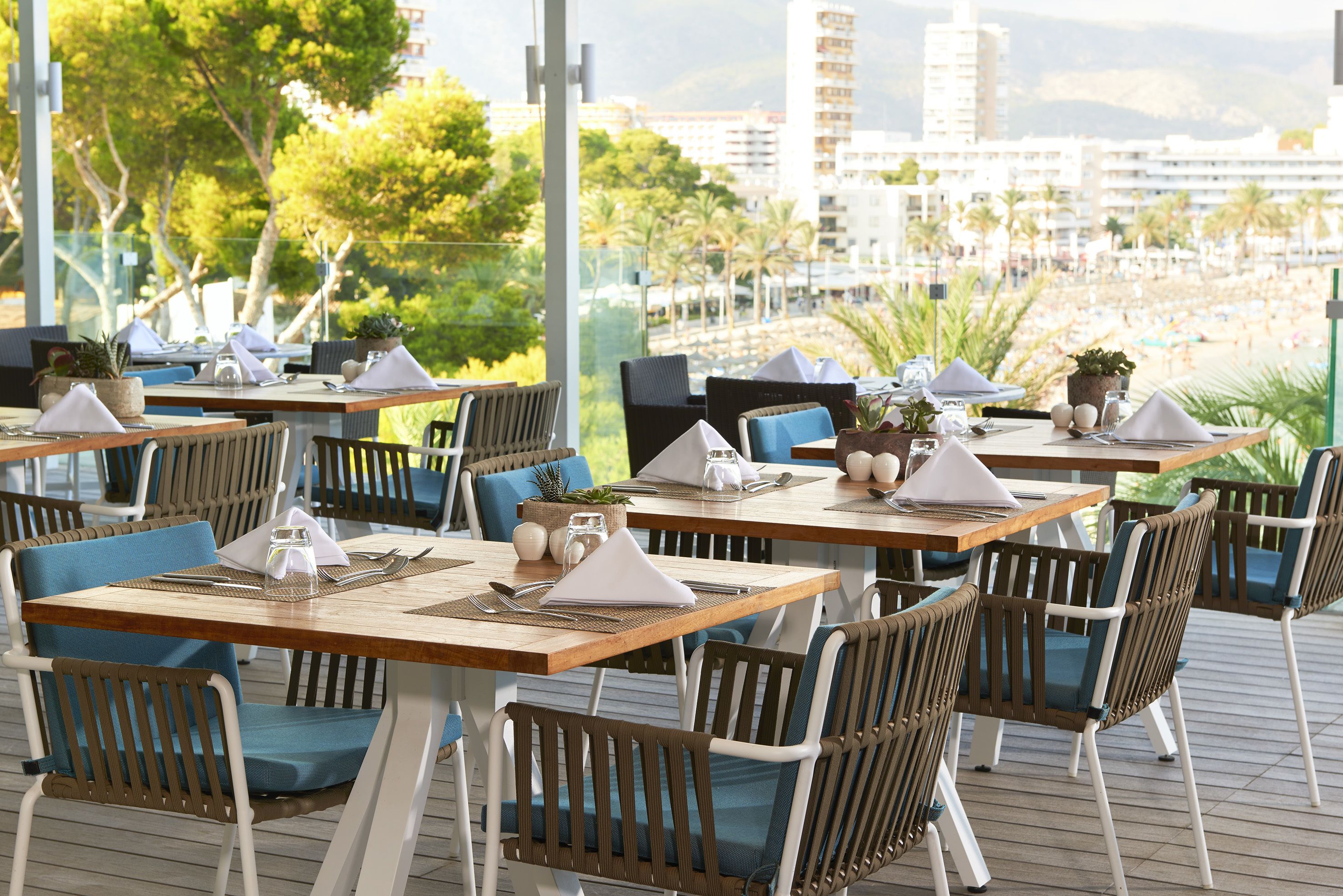 Een restaurant met terras, houten tafels en blauwe stoelen met kussens.