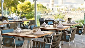 Een restaurant met terras, houten tafels en blauwe stoelen met kussens.