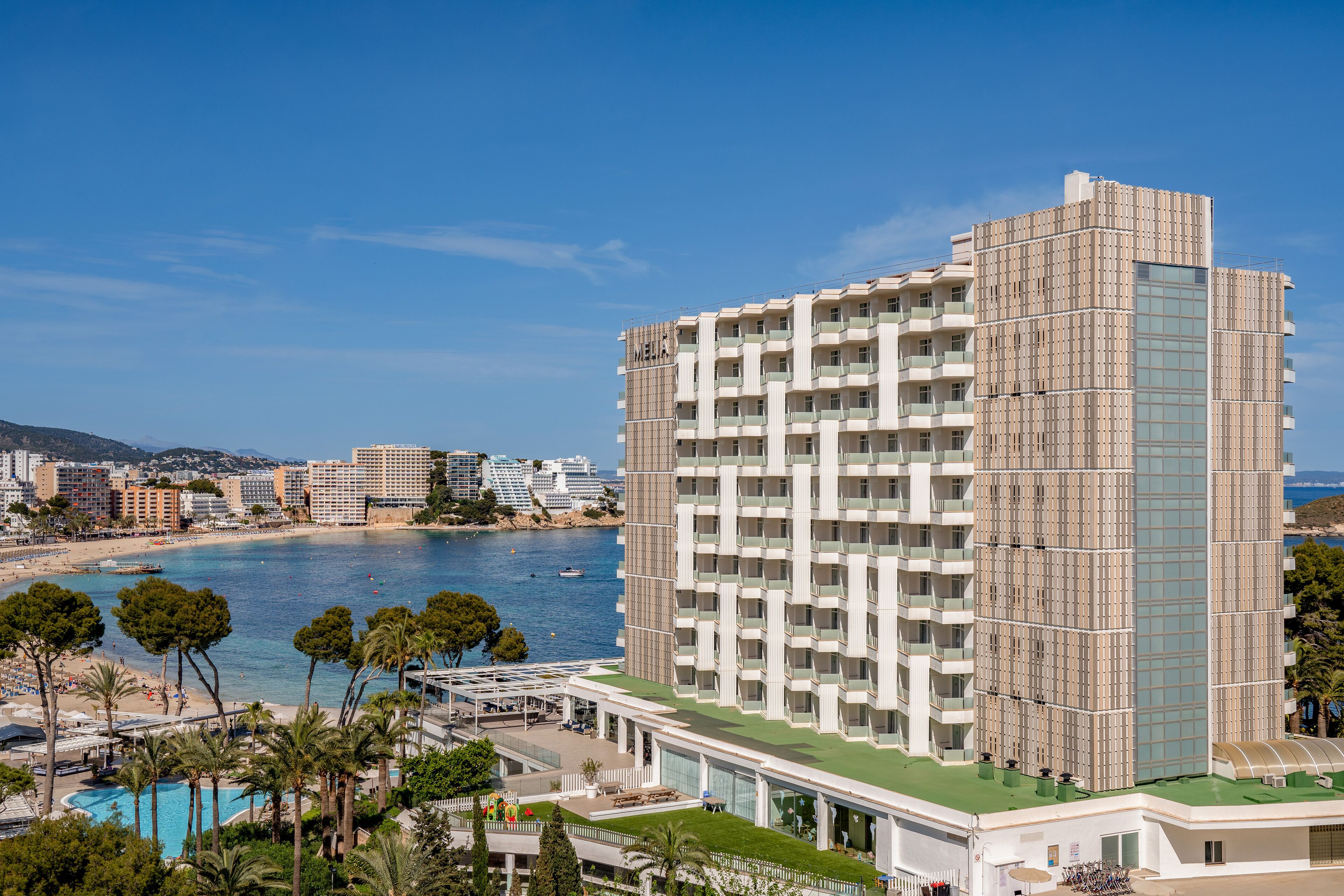 A high-rise hotel with multiple balconies, a pool area, and a view of the sea.
