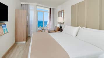 Habitación de hotel con una cama grande, televisión, escritorio con silla y vista al mar a través de un ventanal.