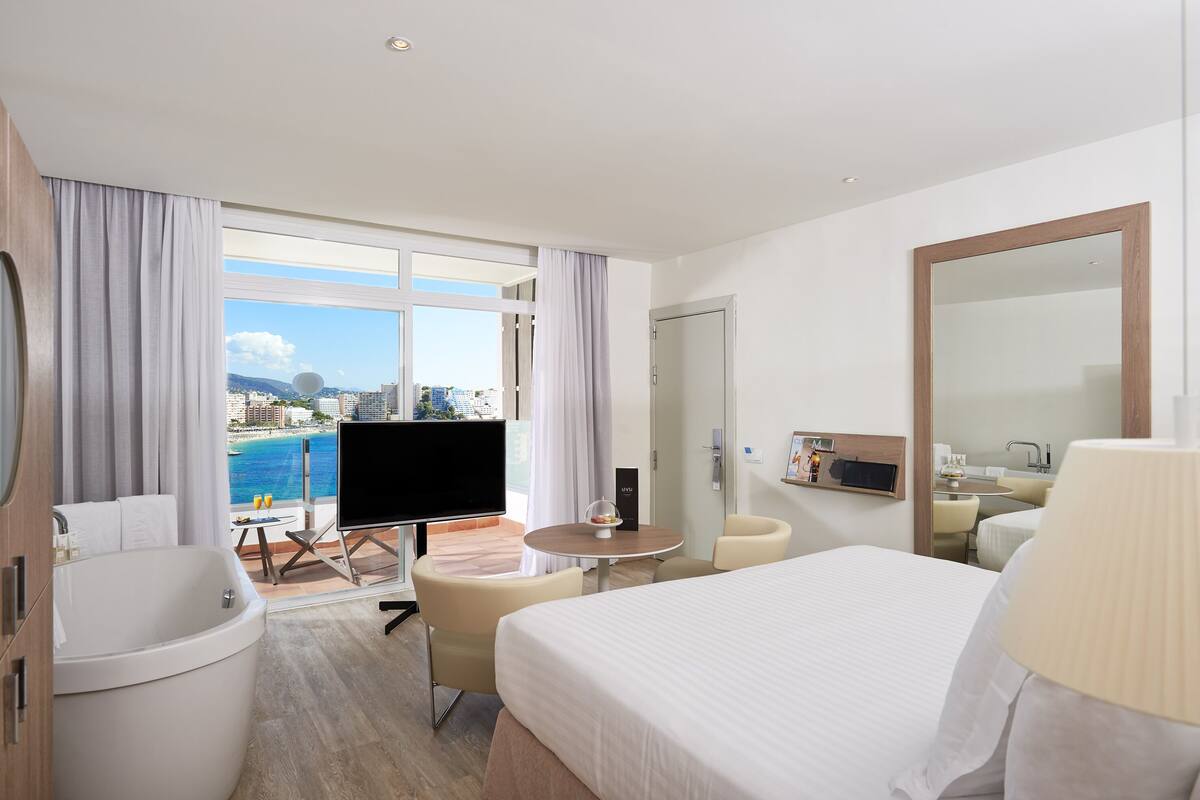 Habitación de hotel con una cama grande, televisión, balcón con vista a la ciudad y baño.